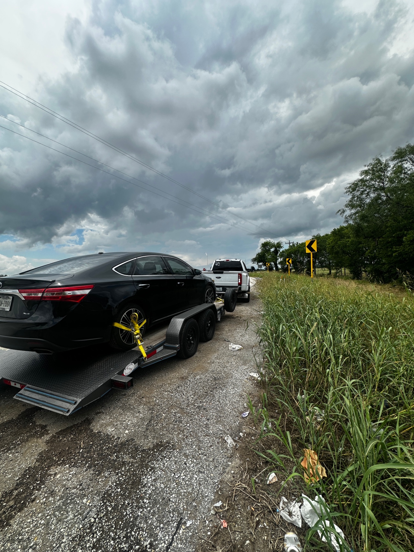 Black sedan strapped to a car-hauler under stormy Texas skies